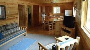 L'intérieur d'une cabine avec un plancher en bois, un canapé, une table à manger avec des chaises, un téléviseur et un ventilateur de plafond.