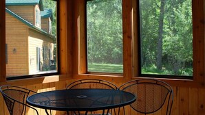 A wooden cabin with a round table and chairs, large windows offering views of a forested area. - Woodland Beach Resort (Deerwood)