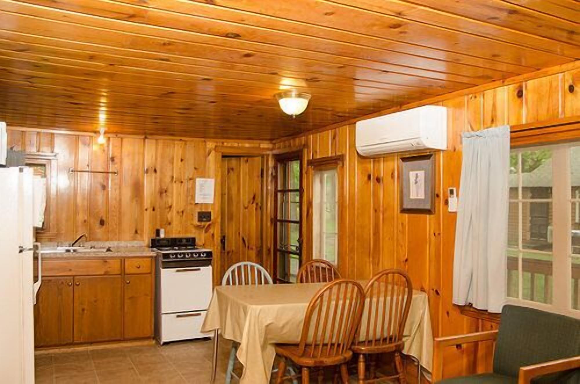 A wooden cabin interior with a kitchen, dining table, and chairs.