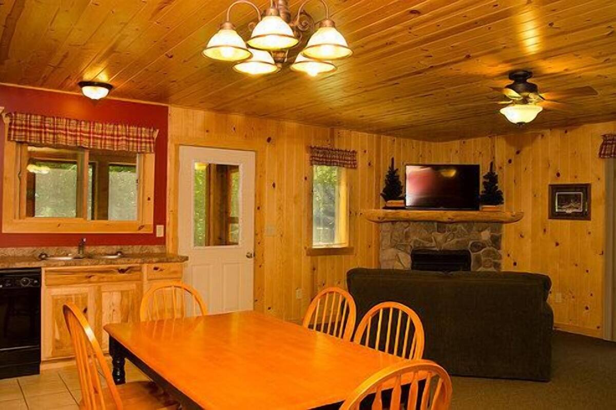 A wooden cabin interior with a dining area, kitchen, and living room.