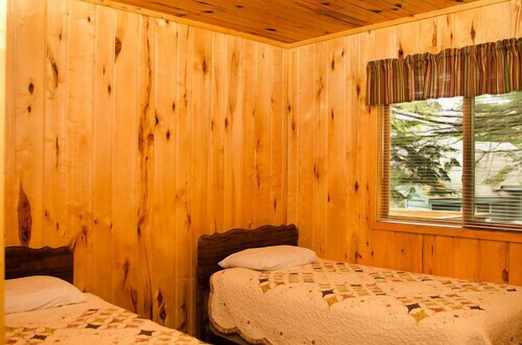 A wooden cabin room with two beds and a window with curtains.