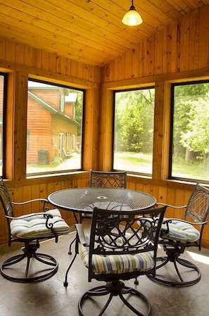 A wooden-paneled room with a round table and four chairs, large windows with a view of a house and greenery outside. - Woodland Beach Resort (Deerwood)