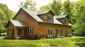 A two-story log cabin with a green roof, a front porch, and a well-maintained lawn. - Woodland Beach Resort (Deerwood)