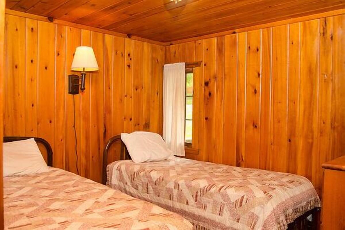 A room with wooden walls and two beds with patterned bedding.