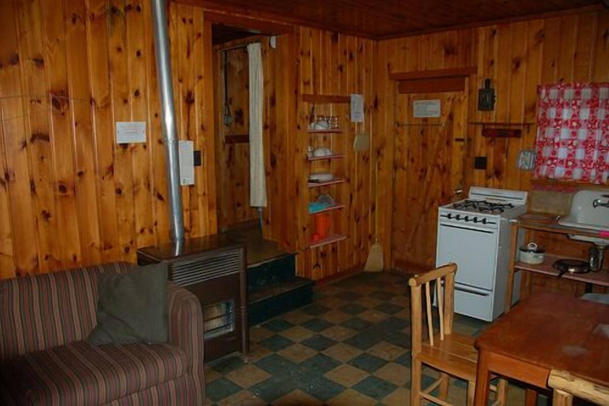 A wooden cabin interior with a sofa, a dining table, a stove, and a sink.