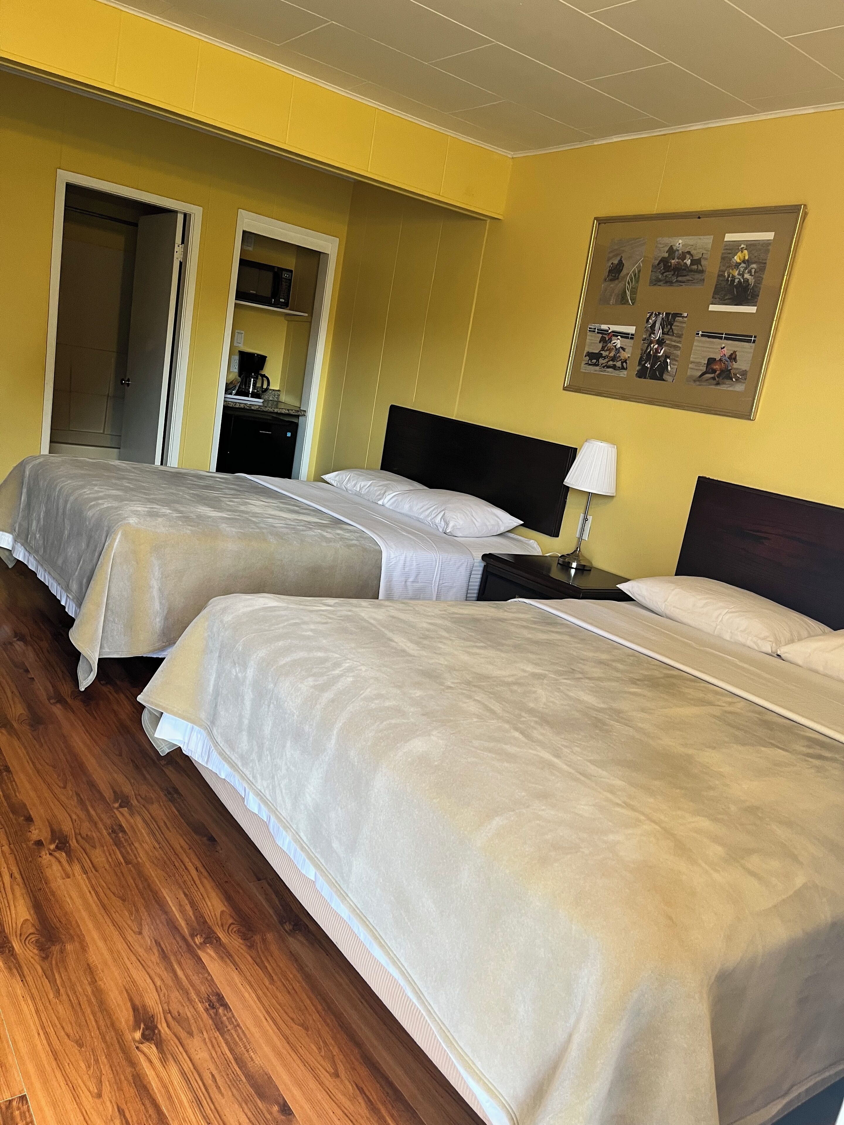 A hotel room with two beds, wooden flooring, a kitchen area, and a framed picture on the wall.