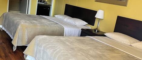 A hotel room with two beds, wooden flooring, a kitchen area, and a framed picture on the wall.