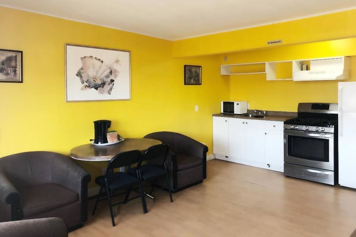 A compact kitchen with white cabinets, a microwave, and a stove. There is a dining area with two chairs and a small table.