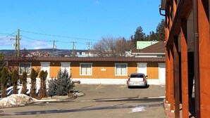 A motel with a parking lot, a single-story building, and a clear blue sky. - Stampeder Motel (Williams Lake)