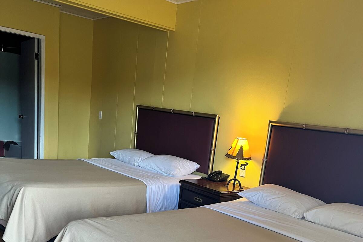A hotel room with two beds, a nightstand with a lamp, and a wooden floor.