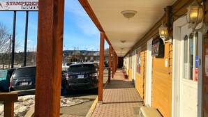 A covered walkway with a sign for Stampeder Motel, parked cars, and a brick-paved path. - Stampeder Motel (Williams Lake)