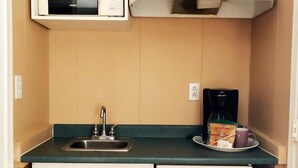 A compact kitchenette with a sink, a microwave, and a coffee maker. - Stampeder Motel (Williams Lake)