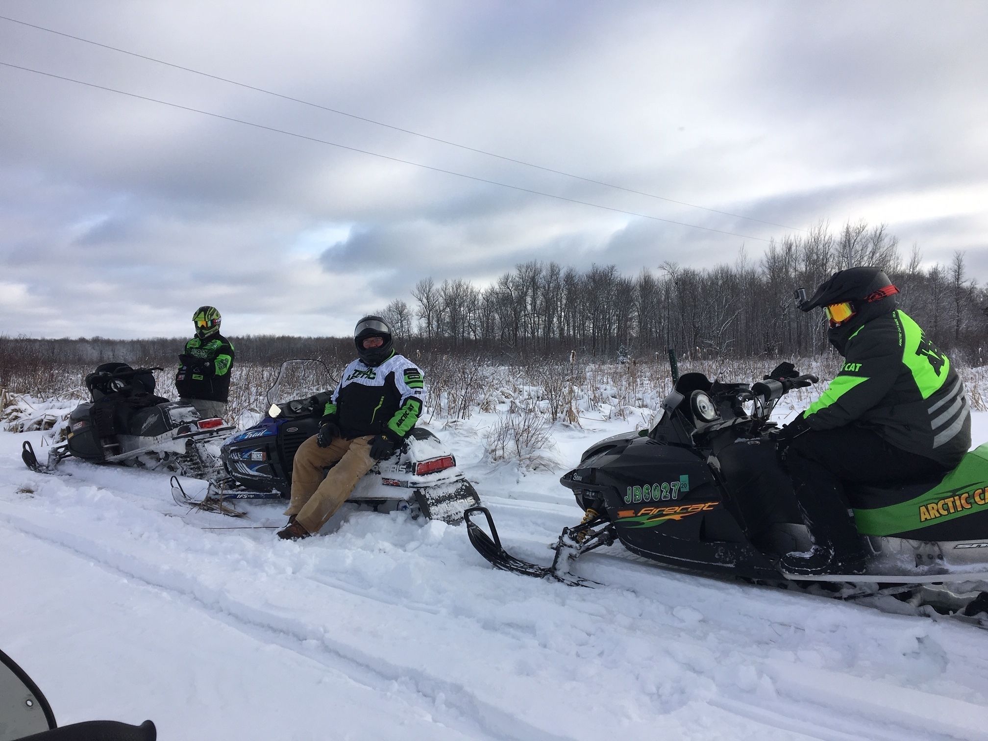 Tres motos de nieve estacionadas en un camino nevado, con un bosque al fondo.