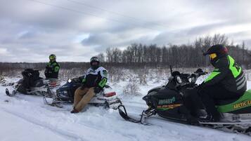 Tres motos de nieve estacionadas en un camino nevado, con un bosque al fondo.