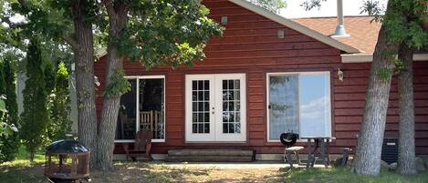 A wooden cabin with a porch, a grill, and a chair.