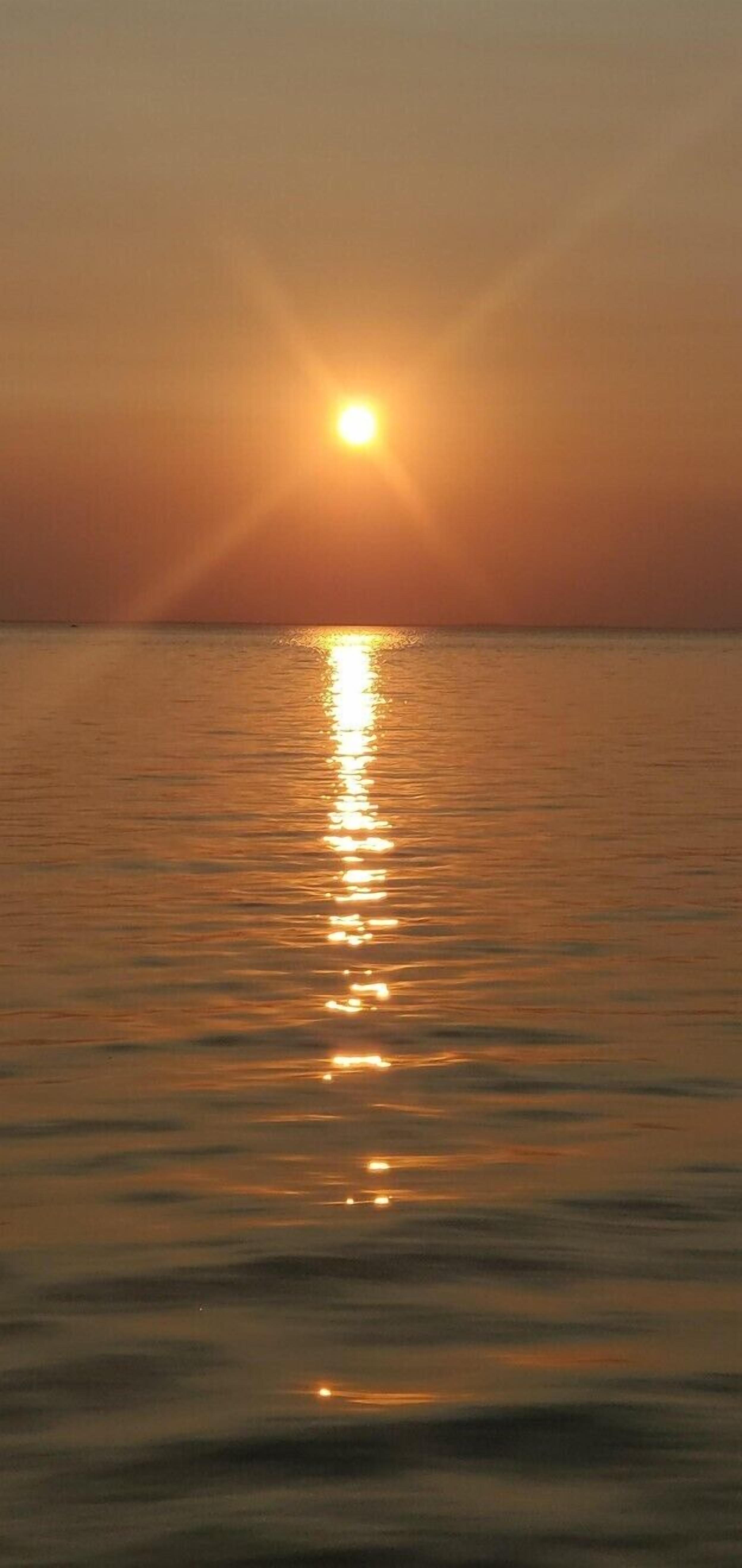 A sunset over a calm body of water with sunlight reflecting on the surface.