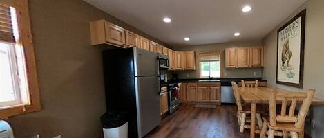 A kitchen with wooden cabinets, a refrigerator, a stove, and a dining table with chairs.