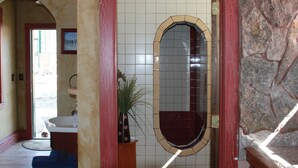 A bathroom with a tiled wall, a sink, a mirror, and a potted plant.