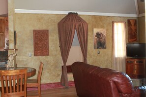Ein Wohnzimmer mit Ledersofa, einem Esstisch mit Stühlen, einem Fernseher und einem dekorativen Vorhang.
