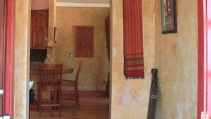 An interior with a wooden dining table, chairs, a hanging tapestry, and a framed picture on the wall.