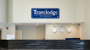 A reception desk with a 'Travelodge by Wyndham' sign, three clocks labeled EST, MST, PST, and a stone-textured counter. - Travelodge by Wyndham Valleyview AB (Valleyview)