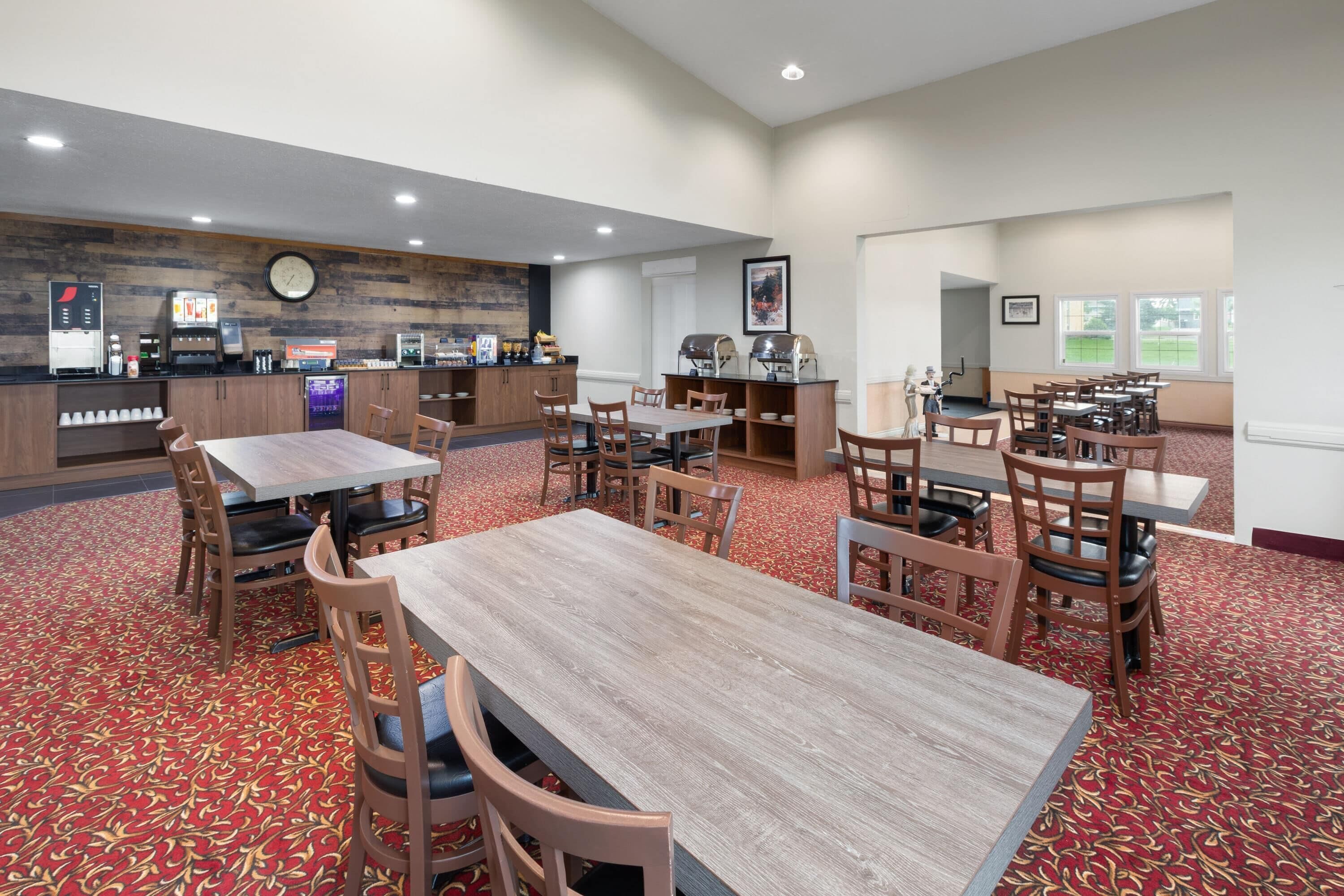 A hotel dining area with multiple tables and chairs, a coffee station, and a clock on the wall.