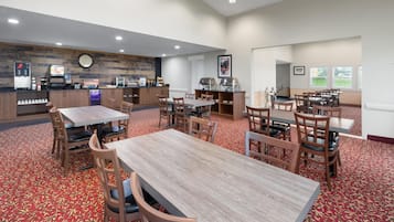 A hotel dining area with multiple tables and chairs, a coffee station, and a clock on the wall.