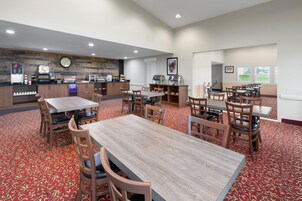 A hotel dining area with multiple tables and chairs, a coffee station, and a clock on the wall.