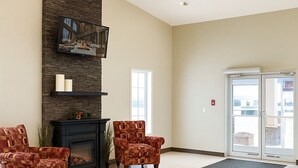 A spacious lobby with a fireplace, two armchairs, a sofa, and a large window. - Travelodge by Wyndham Valleyview AB (Valleyview)