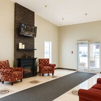 A spacious lobby with a fireplace, two armchairs, a sofa, and a large window.