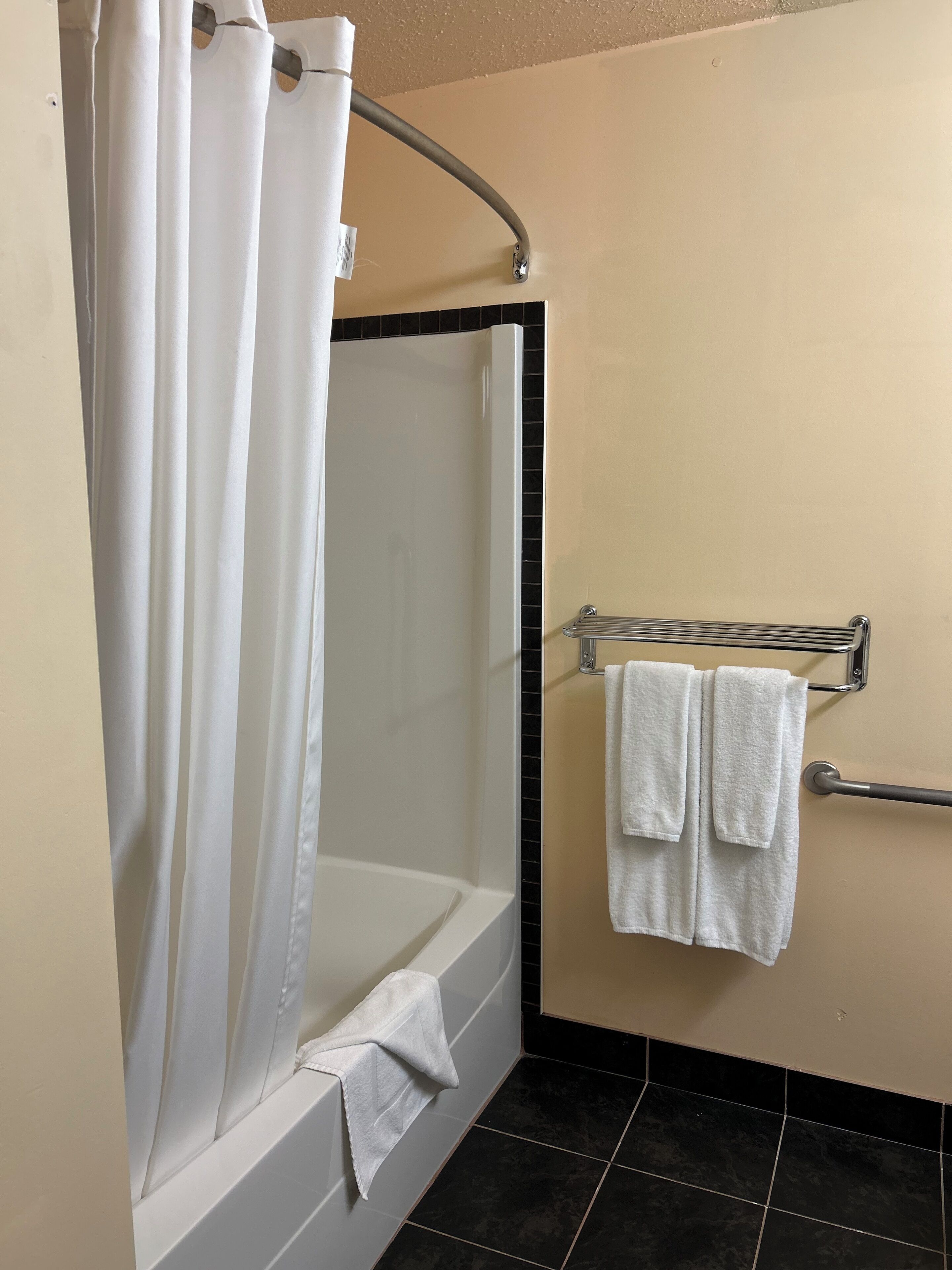 A bathroom with a shower, a towel rack with two towels, and a tiled floor.