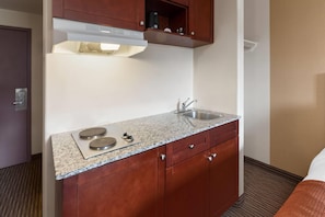 Una kitchenette compacta con un lavamanos de acero inoxidable, dos quemadores y un microondas.