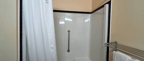 Un área de ducha con puerta de vidrio, cortina blanca y un perchero con una toalla.