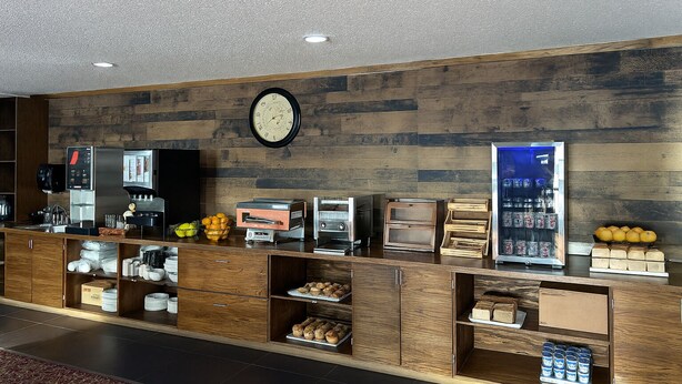 A hotel reception area with a wooden wall, a clock, a coffee machine, a refrigerator, and a display case with oranges. - Travelodge by Wyndham Valleyview AB (Valleyview)