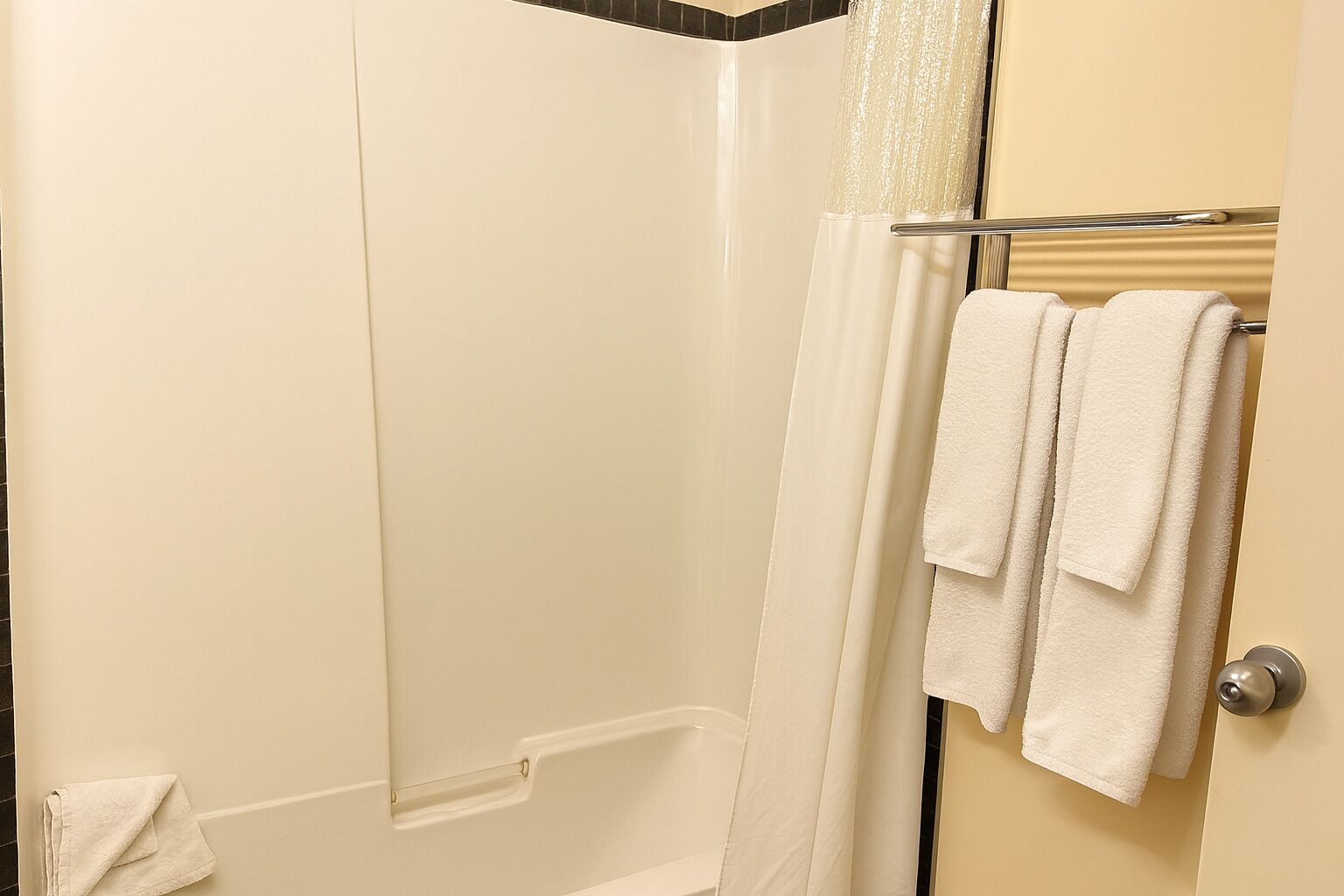 Une salle de bain avec une douche, un porte-serviettes avec deux serviettes et une porte dotée d’une poignée métallique.