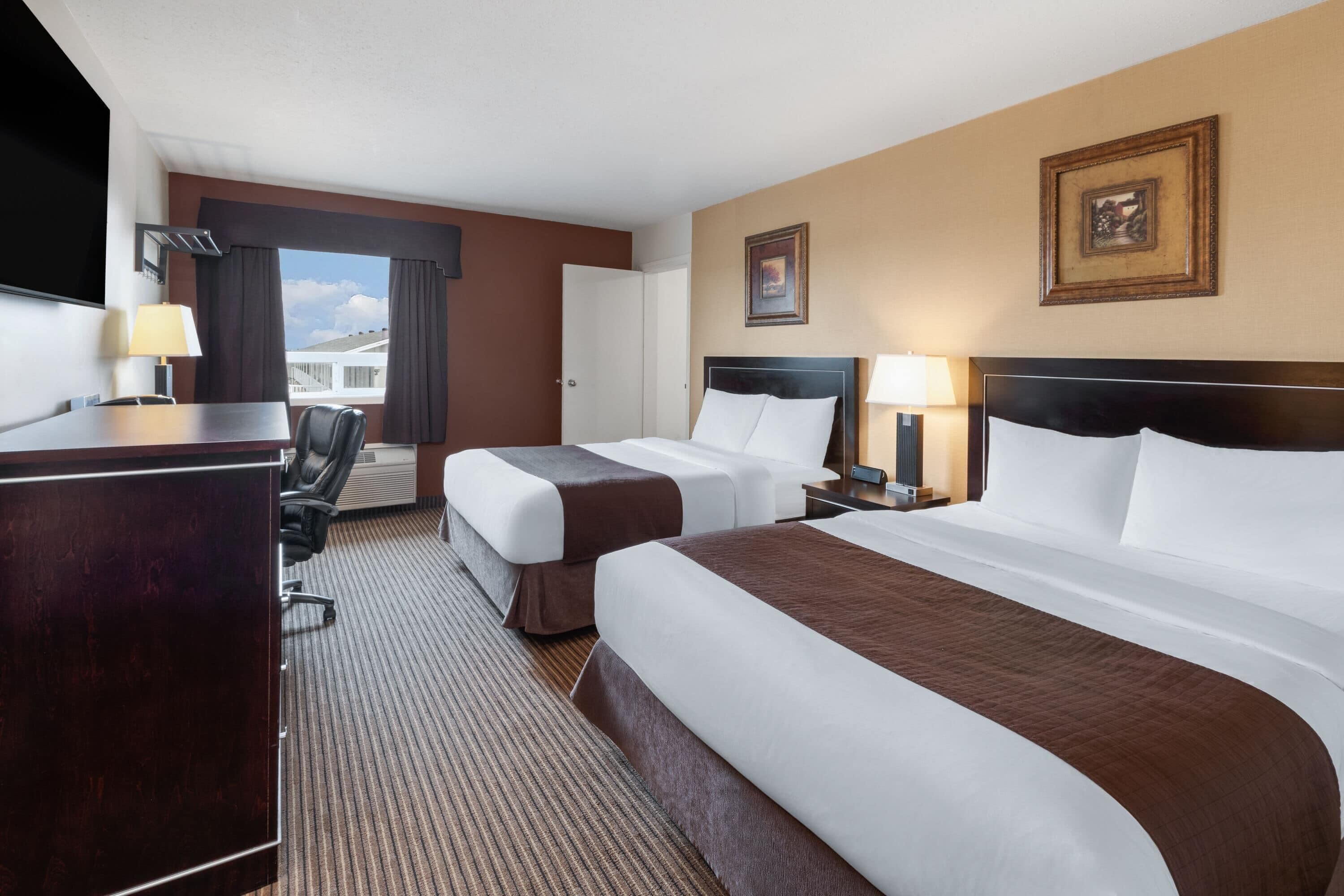 Une chambre d’hôtel avec deux lits, un bureau, une chaise et un téléviseur.