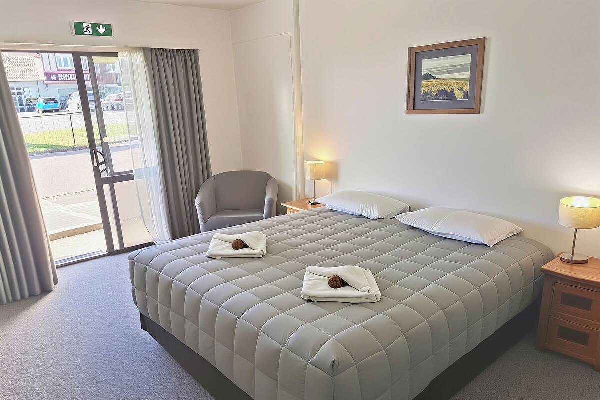 A hotel room with a large bed, two bedside lamps, a chair, and a door leading outside.