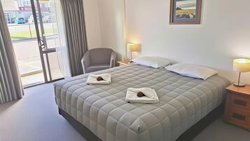 Habitación de hotel con una cama grande, dos lámparas de noche, una silla y una puerta que da al exterior.