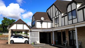 Un bâtiment à deux étages comprenant un espace d’accueil, un parking couvert et une voiture blanche garée devant.