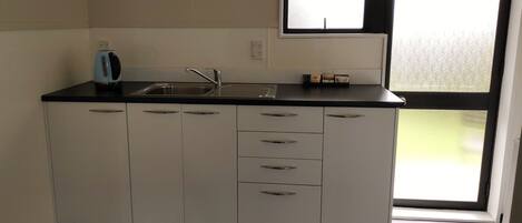 A compact kitchen with a black countertop, white cabinets, a built-in sink, and a window providing natural light.