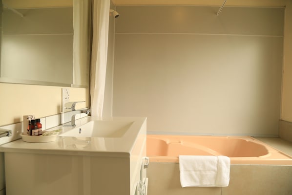 A modern bathroom with a large bathtub, a sink with a mirror, and a towel hanging on the wall.