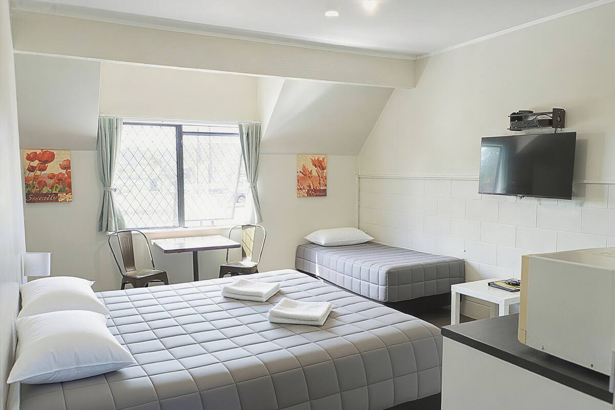 A hotel room with a large bed, a smaller bed, a desk, a chair, a TV, and a window with curtains.