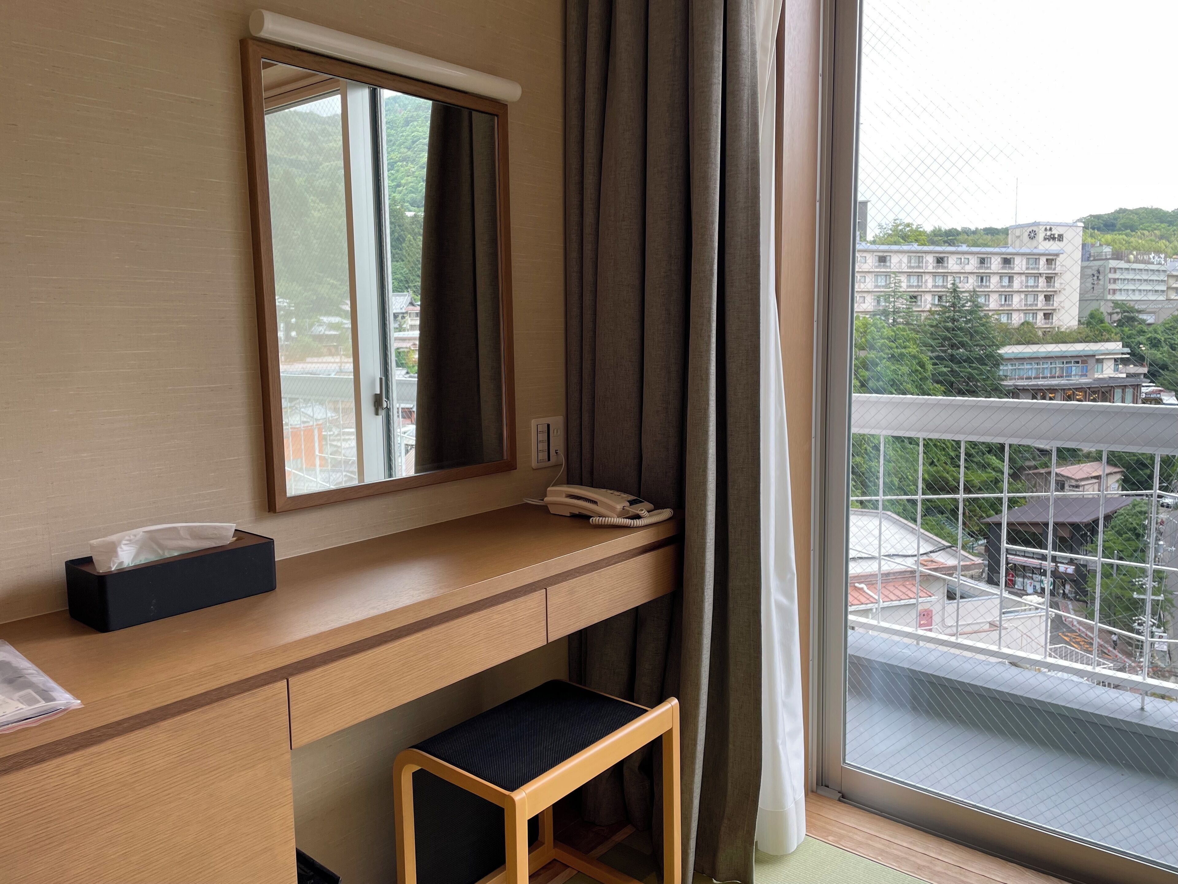 Une chambre d’hôtel avec un bureau en bois, un téléphone, une boîte de mouchoirs et un petit tabouret.