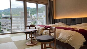 Ein Hotelzimmer mit großem Fenster, einem Bett, zwei Stühlen und einem kleinen Tisch.