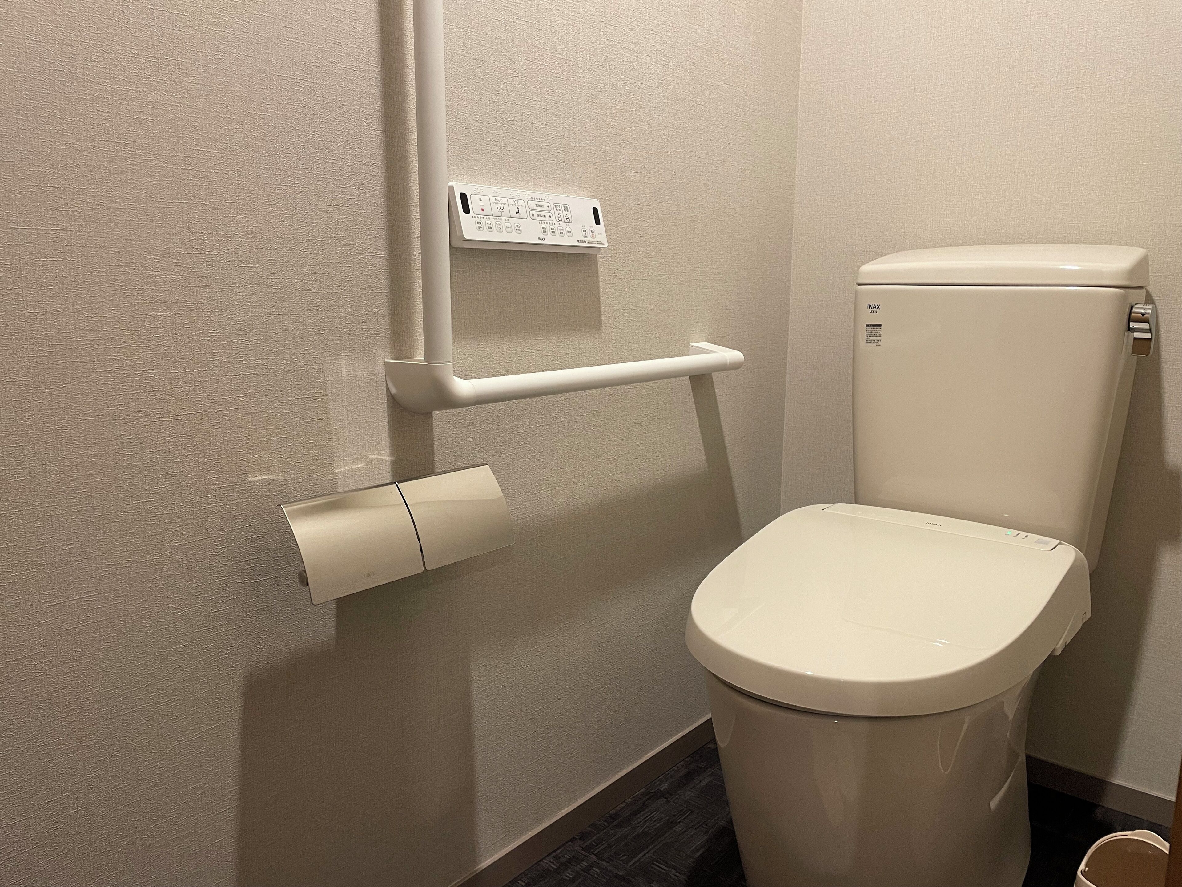 Sanitário com caixa acoplada e tampa brancas, rolo de papel higiênico e painel de controlo fixado na parede.