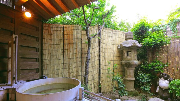 Ein traditionelles japanisches Onsen mit einer Holzterrasse, einem Bambuszaun und einer Steinhlaterne.