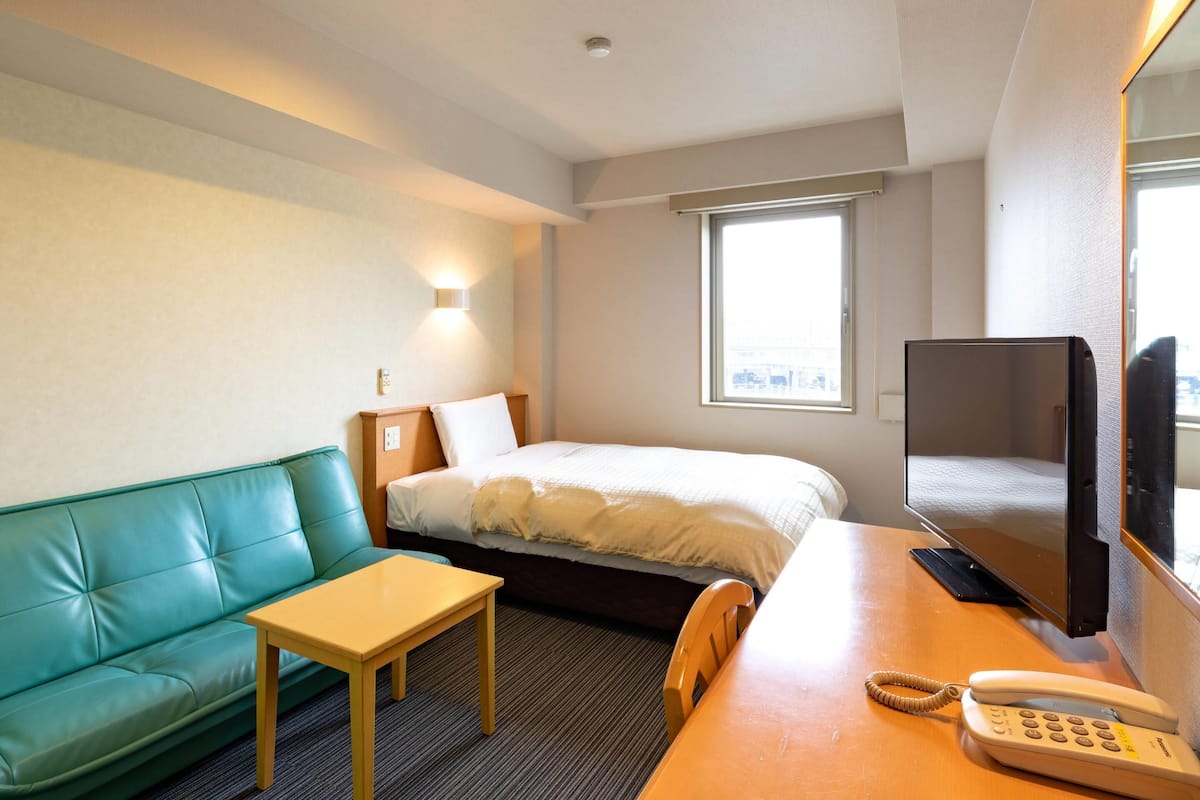 A hotel room with a bed, a green couch, a small table, a desk with a telephone, and a television.