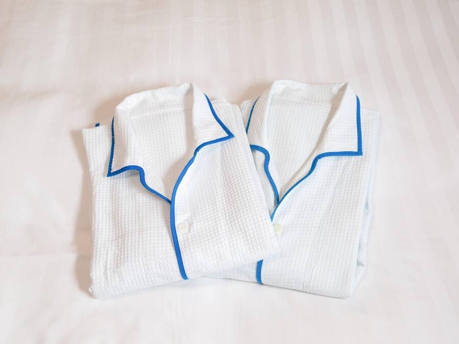 Des robes blanches, soigneusement pliées, avec une bordure bleue, sont posées sur un lit.