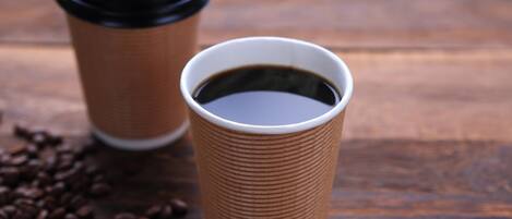 Two coffee cups on a wooden surface with scattered coffee beans.