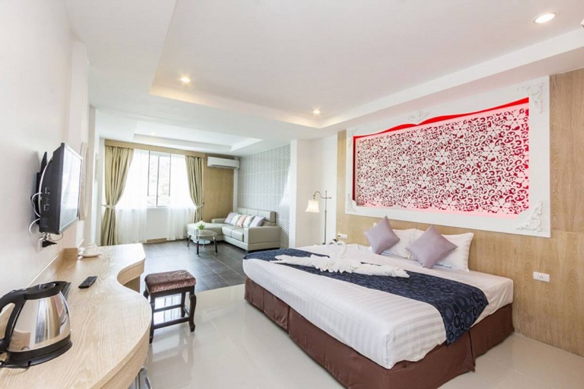 A hotel room with a bed, a desk with a kettle, a TV, and a large decorative wall piece.